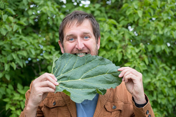 a bearded man bites a leaf of a plant against the background of foliage
