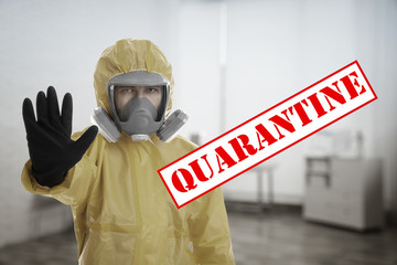 Man in chemical protective suit showing STOP gesture indoors. Prevention of virus spread
