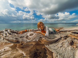 A girl in a bikini lies on a wooden log on the sandy beach of a tropical spree on a sunny day