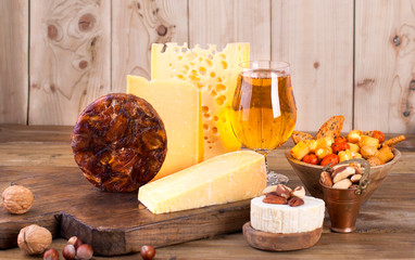 different cheese classic choice, on an old wooden board, nuts, snacks and a glass of beer. Traditional Dutch cheese of different varieties. Free space for text.