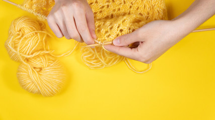 Women's hands knit from yellow wool on a yellow background, top view. Hand knitting