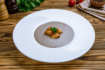 Cream soup of mushrooms on white plate on wooden table