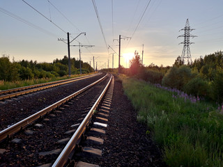 Fototapeta na wymiar Railroad rails and electric wires in the summer on sunset background