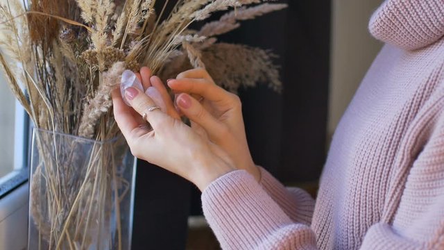Female hands holding two yoni eggs made from pink quartz and transparent violet amethyst for vumfit, imbuilding or meditation near the window with vase of spikelets.