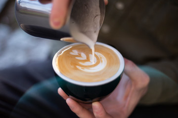 Barista makes latte art drawing on cappuccino coffee.