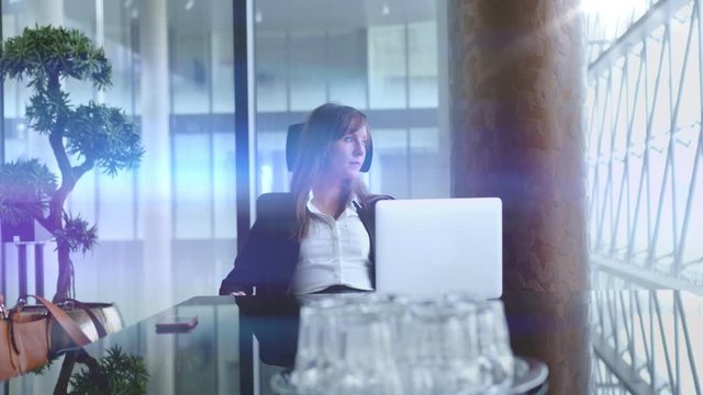 Businesswoman working at desk with laptop computer in corporate office, thinking, waiting for partners in meeting room. 4K video footage.