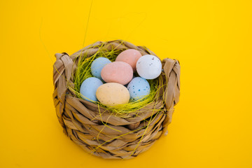 Easter holiday decorations on yellow background. Colorful easter painted speckled eggs in basket. Creative spring composition with Easter elements - flowers and eggs. Traditional Easter Celebrating