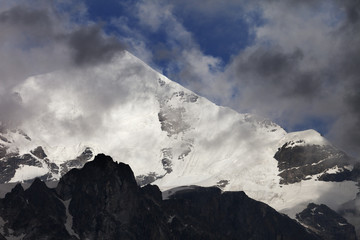 High snowy mountains with glacier, rocks and blue sky with dark clouds before storm