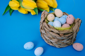 Happy Easter. Easter holiday decorations on trendy colored classic blue background. Creative spring composition with Easter elements - flowers and eggs in basket. Celebrating Easter concept at spring