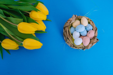 Fototapeta na wymiar Happy Easter. Easter holiday decorations on trendy colored classic blue background. Creative spring composition with Easter elements - flowers and eggs in basket. Celebrating Easter concept at spring