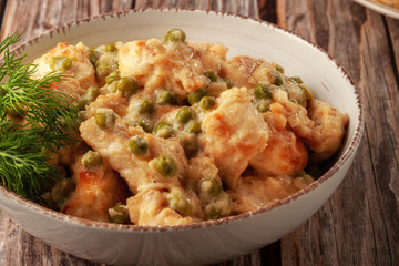 Braised chicken fillet with green peas on a wooden table