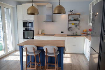 White, well lit scandi kitchen with blue island and double brass pendant lights.