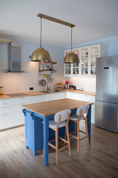 White, well lit kitchen with blue island and double brass pendant lights.. Vertical shot.