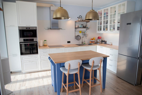 White, bright scandi kitchen with blue island and double brass pendant lights.