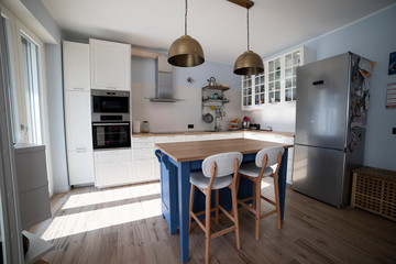 White, bright, scandi kitchen with blue island and double brass pendant lights.