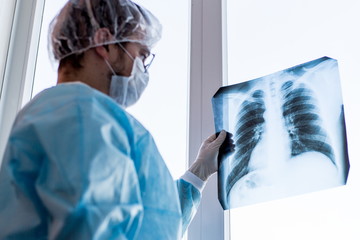 Doctor in a protective mask during the quarantine period for the spread of coronavirus. Holding a chest x ray while standing in the hospital checking for illnesses