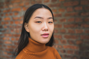 Asian woman against brick wall.