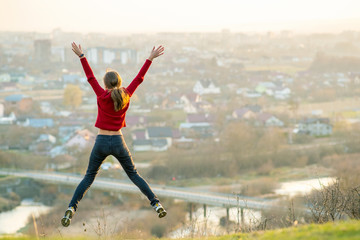 Fototapeta na wymiar Young woman jumping with outstretched arms and legs outdoors on a distant city background. Relaxing, freedom and wellness concept.