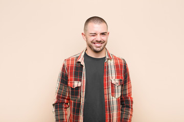 young handsome man looking happy and friendly, smiling and winking an eye at you with a positive...