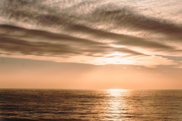Beige sunset over the sea. The sun comes out from behind a undulating cloud over a quiet surface of the water