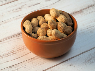 Dried peanuts in clay bowl, on wooden background