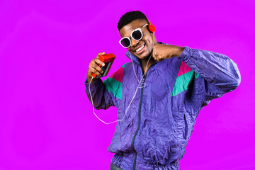 African American young man, in a jacket in the style of the 90s, with a retro cassette player, hears music, the mood of dancing and fun, yellow and purple colors