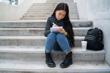 Asian woman writing on notebook.