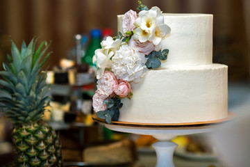 Tall sweet wedding cake decorated with live pink and white flowers on a table.