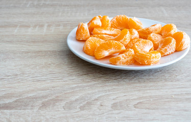 Pealed mandarin peaces on white plate, wooden desk surface