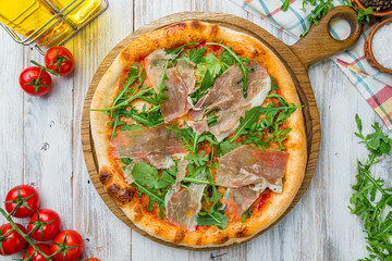 Pizza with Parma ham and arugula on white wooden table