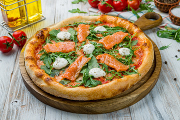 Pizza with salmon and Philadelphia cheese and aragula on white wooden table
