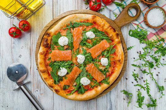 Pizza with salmon and Philadelphia cheese and aragula on white wooden table