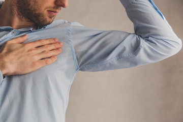 Man with hyperhidrosis sweating very badly under armpit in blue shirt, on grey. - obrazy, fototapety, plakaty