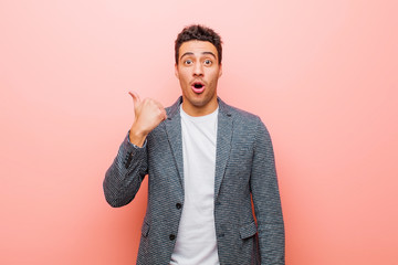 young arabian man looking astonished in disbelief, pointing at object on the side and saying wow,...