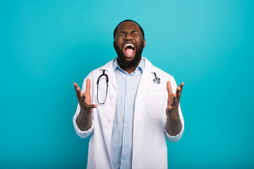 Exhausted doctor with lab coat and stethoscope screams on cyan background