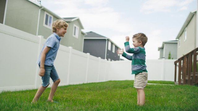Young boy taunts and pushes his big brother, who chases him across the yard