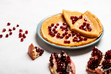 Pancakes with pomegranate and condensed milk lie on a plate. Close-up.