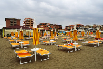 Lined up sunbeds on a deserted beach on a cloudy day. Tuscany