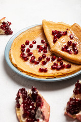 Pancakes with pomegranate and condensed milk lie on a plate. Close-up.