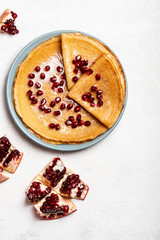 Pancakes with pomegranate and condensed milk lie on a plate. Close-up. Copy space for text. Top view.