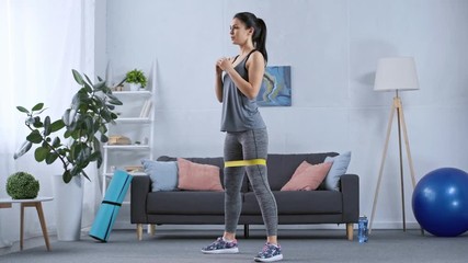 Sportswoman doing squats with resistance band while training at home - Powered by Adobe