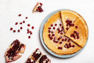 Pancakes with pomegranate and condensed milk lie on a plate. Close-up. Top view.