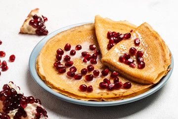 Pancakes with pomegranate and condensed milk lie on a plate. Close-up.