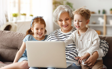 Happy aged woman with grandchildren using laptop at home