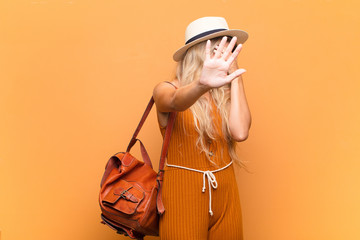 young pretty latin woman covering face with hand and putting other hand up front to stop camera,...