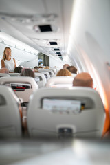 Pretty, young woman aboard an airplane during a lang haul commercial flight - stretching her legs a bit, walking in the aisle