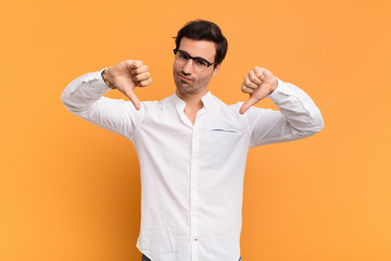 young handsome man looking sad, disappointed or angry, showing thumbs down in disagreement, feeling...