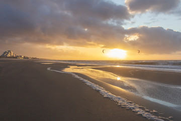 View of the north sea beach on a windy winter day at sunset, people, kitesurfing. Noordwijk, the Netherlands