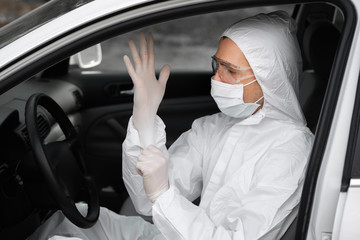 Man in protective suit, medical mask and rubber gloves for protect from bacteria and virus is planning to drive. Protective mask while quarantine, world pandemic, covid 19, coronavirus, infection.