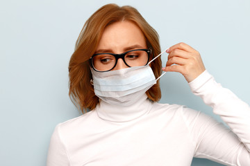 Studio portrait of woman in glasses wearing face medical mask, looking at camera, isolated on blue background. Flu epidemic, dust allergy, protection against virus. Covid-19, coronavirus pandemic
